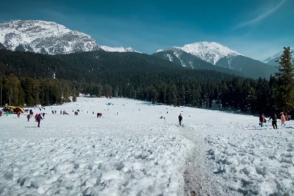 A picturesque view of Baisaran Valley in winter, covered with snow, with tourists enjoying the landscape, surrounded by pine trees and snow-capped mountains